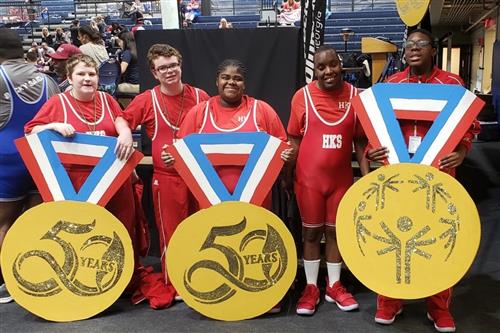 Team members stand in a group with large medal displays 