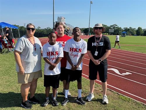 Coaches and athletes stand next to the track posing for a picture. 