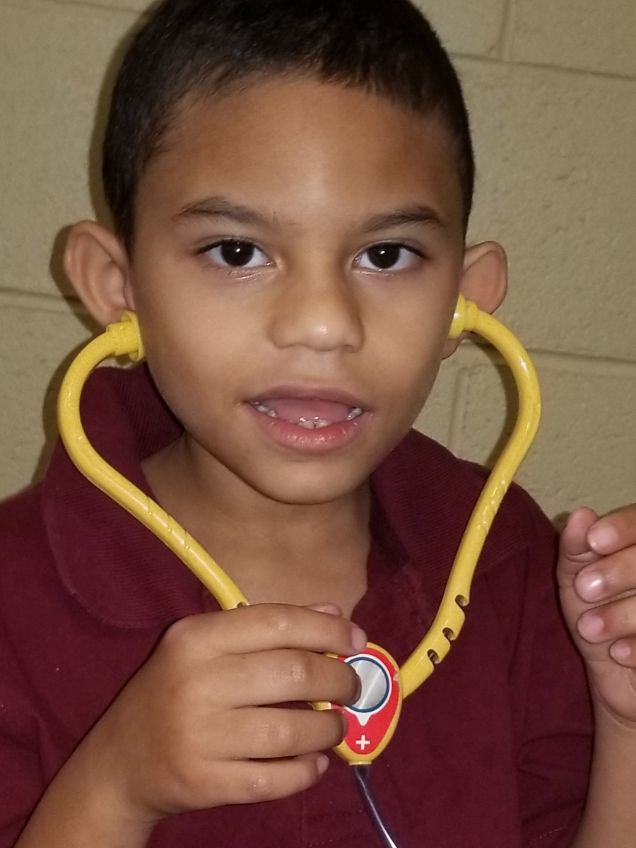 A young, male student holding a toy stethoscope up to his ears. 