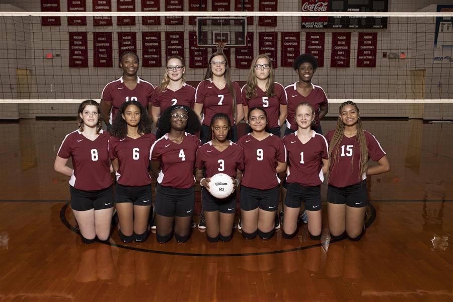 ASD varsity volleyball team stand side by side in the gym.