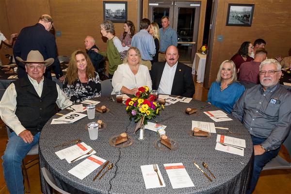 Six people seated at a table smile at the camera.