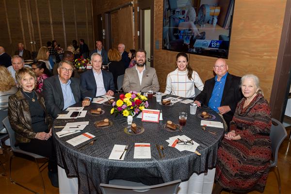 Seven people seated at a table are smiling at the camera.