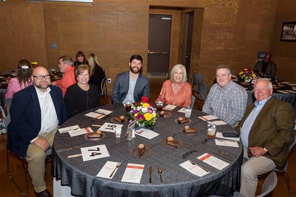  Six people seated around a table smile at the camera.